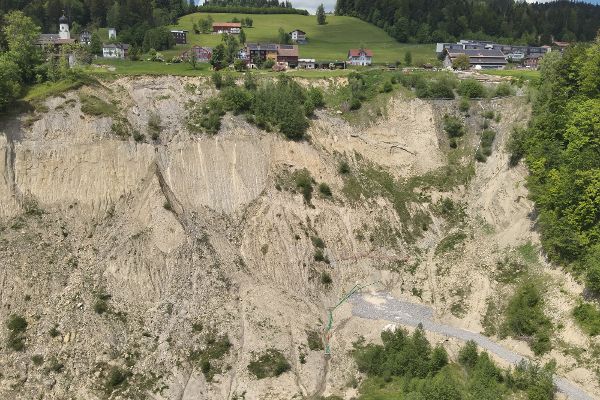 Am oberen Rand einige Häuser in der Landschaft, knapp darunter eine große, steile, steinig-erdige Fläche, bei der es zu einer Rutschung gekommen ist.