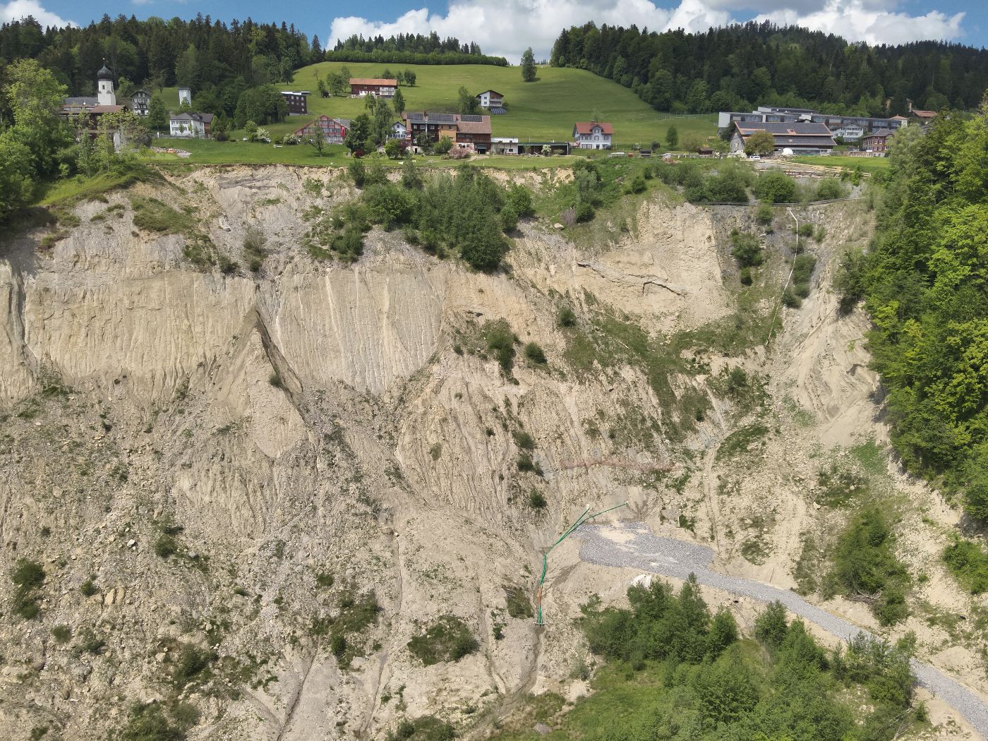 Am oberen Rand einige Häuser in der Landschaft, knapp darunter eine große, steile, steinig-erdige Fläche, bei der es zu einer Rutschung gekommen ist.