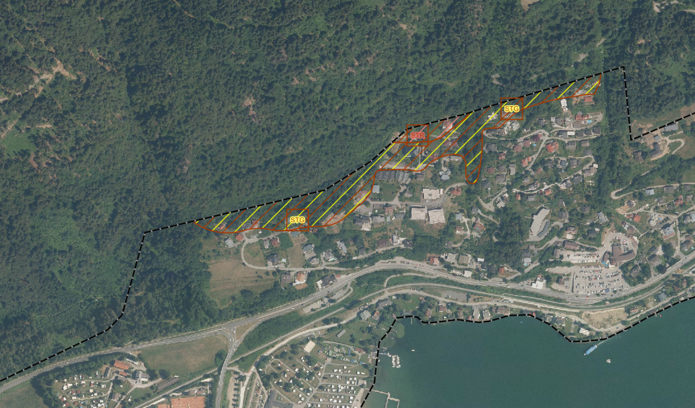 Der Kartenausschnitt zeigt einen braunen Hinweisbereich unterteilt in braun-gelbenschraffierten und braun-rotenschraffierten Bereichen in der Treffen am Ossiacher See. Die Abkürzungen STR steht für Steinschlag rote Zone (hohe Gefahr) und STG für Steinschlag gelbe Zone (geringere Gefahr). 